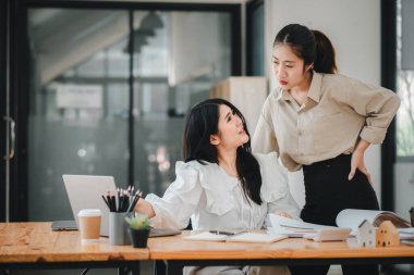 Ofisteki bir tartışmada iki profesyonel kadın, biri oturuyor ve diğeri ayakta, ortak bir iş ortamında..