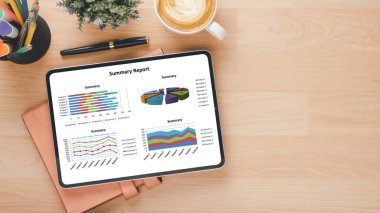 Renkli kırtasiye malzemeleri, bir defter ve bir latte ile çevrili bir özet rapor gösteren bir tablet ile işyeri kurulumu.