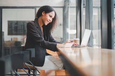 Güneşli bir kahve dükkanında çalışırken gülümseyen kendine güvenen genç girişimci başarılı bir uzaktan çalışma örneği gösteriyor..