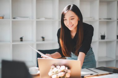 Gülümseyen kadın internetten alışveriş yapıyor. Kredi kartı ve laptopuyla. Etrafı aydınlık, modern bir ofis alanı ile çevrili..