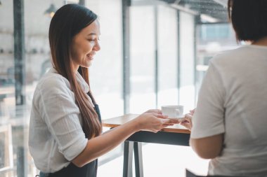 Sıcak, cezbedici bir kafe atmosferinde müşteriye sıcak bir gülümsemeyle kahve servisi yapan arkadaş canlısı barista..