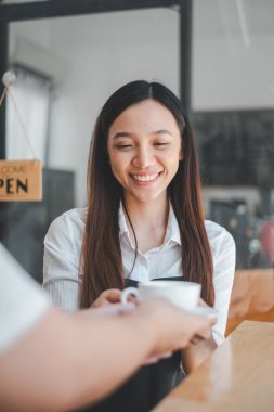 Sıcak, cezbedici bir kafe atmosferinde müşteriye sıcak bir gülümsemeyle kahve servisi yapan arkadaş canlısı barista..