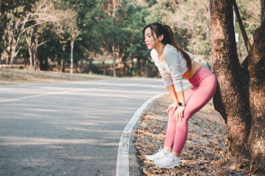 Bir koşucu hak ettiği molayı alır, bir ağaca yaslanır manzaralı bir parkta soluklanırken, fitness yolculuğunda dinlenme anını ön plana çıkarır..