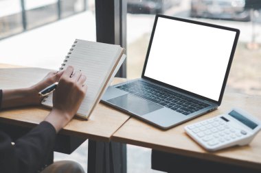 Kişi, parlak, modern bir çalışma alanındaki iş planlama, bütçe veya finansal analizlere odaklandığını belirten bir hesap makinesiyle şık bir dizüstü bilgisayarın yanına özenle bir not defteri yazmaktadır..