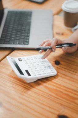 Ahşap bir masa üzerinde dizüstü bilgisayarın yanında hesap makinesi kullanan eller, mali çalışmayı veya çalışmayı gösterir..