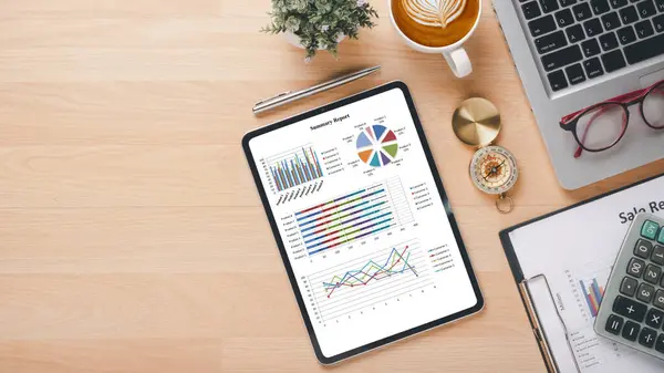 Organized workspace with a digital tablet showcasing colorful business analytics, a cup of coffee, and office supplies.