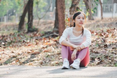 Güneşli bir sabahta kadın koşucu antrenmandan sonra dinleniyor. Şehirdeki gölet boyunca caddede oturan kadın fitness modeli. Koşu antrenmanına ara veren bayan koşucu.