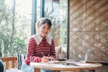 Çalışkan kadın, dizüstü bilgisayarı güneşli bir kafe masasında açık not defterine dalmış..