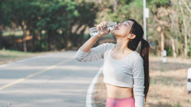 Spor yaptıktan sonra şişeden su içen genç bayan sporcu, doğal park ortamında kendini yeniliyor..