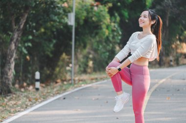 Neşeli genç kadın huzurlu bir yolda bacak esnetiyor, doğanın ortasında sabah sporunun keyfini çıkarıyor..