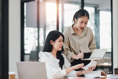 İki profesyonel kadın, parlak ve modern ofis ortamında bir projede işbirliği yaparken neşeli bir anı paylaşıyorlar..