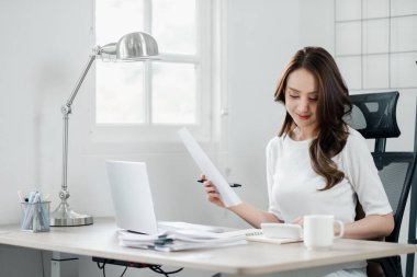 Genç bayan, iyi organize edilmiş işyerindeki bir belgeyi dikkatle inceliyor..