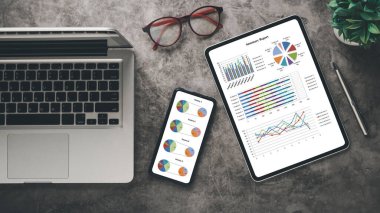 Pürüzsüz bir çalışma alanı dizüstü bilgisayar, özet raporlu tablet, çizelgeli akıllı telefon, gözlük ve yeşil bitki..