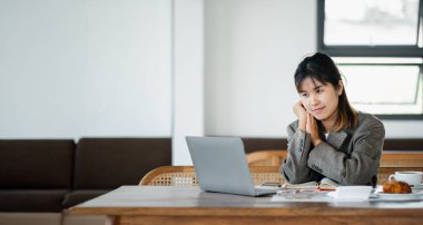 Diz üstü bilgisayardaki işi incelerken, rahat bir kafe ortamında düşünceli bir iş kadını..