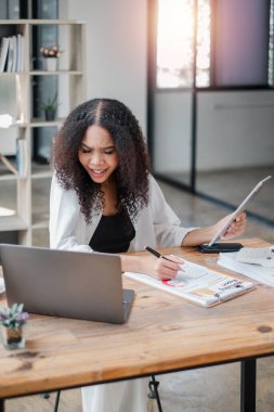 Masasında hesap makinesi ve dizüstü bilgisayarla evrakları inceleyen genç bir profesyonel kaygılı. Muhtemelen mali raporları inceliyor..