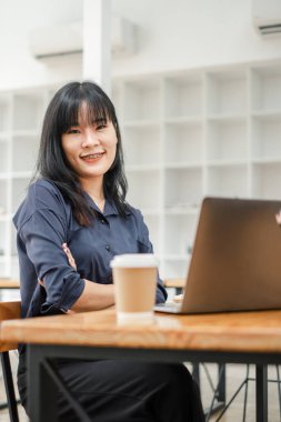 Kameraya gülümseyen diş telleri olan profesyonel bir kadın, iyi ışıklandırılmış bir ofis alanında dizüstü bilgisayarla oturuyor..