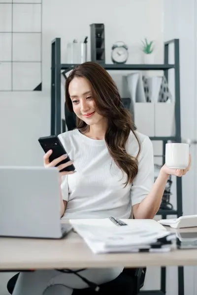 Businesswoman Checks Her Smartphone While Holding Cup Coffee Laptop Open Royalty Free Stock Images