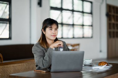 Serbest Çalışan, bütçesini, kahvesini ve pastanesini planlarken düşünceli bir bakışla bir kafedeki dizüstü bilgisayardan hesaplarını değerlendiriyor..