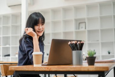 Diş teli takan mutlu genç öğrenci, parlak ve modern bir çalışma ortamında dizüstü bilgisayarının önünde dikkatle çalışıyor..