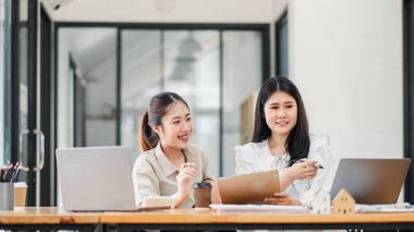 Gündelik iş kıyafetleri içinde gülümseyen iki kadın profesyonel iyi ışıklandırılmış, çağdaş bir ofiste pano üzerinde tartışıyorlar..