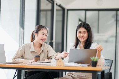 İki kadın bir dizüstü bilgisayarla arkadaşça bir tartışmaya girişirler, biri ekranı işaret eder, biri kahve ve kırtasiyeli bir ofis masasında..