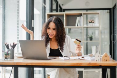 Bilgisayarı kullanırken kredi kartı tutan kafası karışmış bir kadın, muhtemelen online ödeme sorunuyla karşı karşıya..