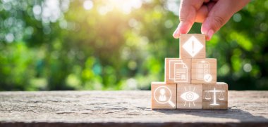 Uyum kavramı, el ele tutuşan ahşap blok üzerinde kurallar, standartlar, yönetim, şeffaflık, vizyon ve sanal ekranda hukuk simgesi. 