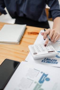 İş raporları üzerinde hesap makinesi kullanarak ahşap bir masanın üzerinde defter ve akıllı telefon kullanarak ellerinizi yakın plan çekin..