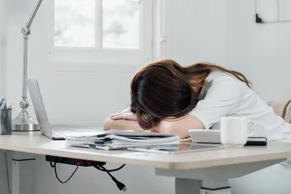 Exhausted professional takes a quick power nap at her desk, amidst a busy work schedule.
