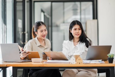 Ofis masasında dizüstü bilgisayarları ve belgeleri olan bir proje üzerinde çalışan profesyonel kıyafetli iki kadın..