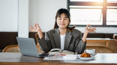 Profesyonel kadın yoğun bir programın ortasında huzur bulmak için çalışma masasında meditasyon yapıyor..