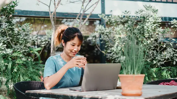 Woman Blue Top Sipping Coffee While Using Laptop Garden Table Stock Image