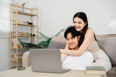 Genç bir kadın, dizüstü bilgisayar ekranına odaklanırken, her ikisi de mutlu bir şekilde gülümseyen bir adama sarılıyor..