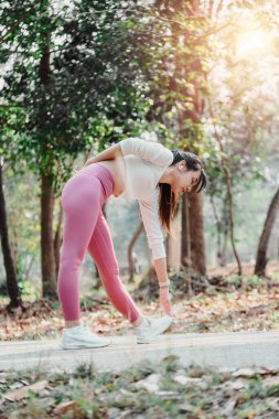 Aktif genç bir kadın güneşli bir orman parkında bacaklarını açmak için mola veriyor.