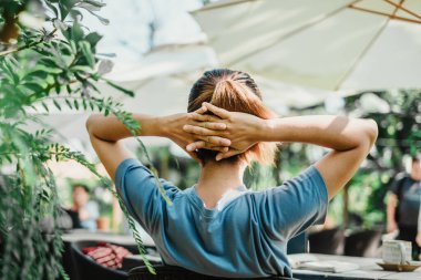 Rahatlatıcı bir moladan hoşlanan kişi, ellerini başının arkasına sıkıştırmış, açık bir bahçe alanının huzurlu yeşilliğinin ortasında.