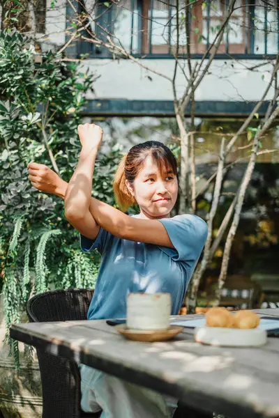 stock image Woman takes a stretch break at her garden table workstation, surrounded by lush greenery and a relaxing outdoor ambiance.