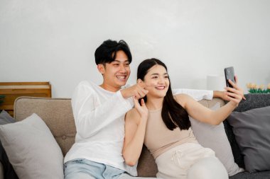 Neşeli genç çift oturma odasındaki kanepede rahatça uzanırken selfie çekerek neşeli bir anı yakalıyorlar..