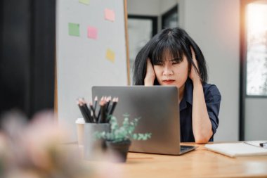 İş kadını, modern ofis ortamında dizüstü bilgisayarında çalışırken stresli ve bitkin görünüyor..