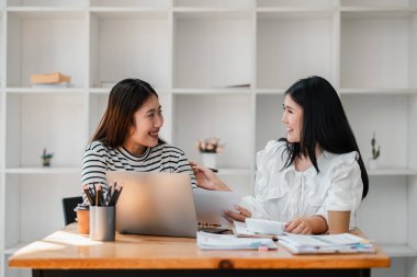 Çağdaş bir ofiste dostane bir tartışmada iki kadın iş arkadaşı, belgeler ve bir dizüstü bilgisayar hakkında fikir alışverişinde bulunuyor..