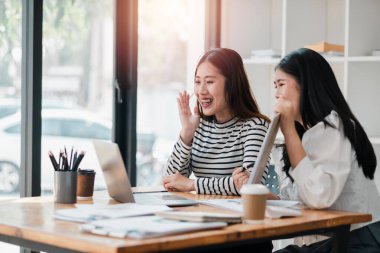 İki bayan meslektaşın verimli bir ofis toplantısı sırasında masadaki belge ve laptopla kahkahalar attığı neşeli bir an..
