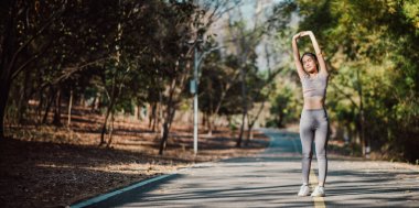 Aktif genç kadın kollarını uzatıyor, sakin bir park yolunda sabah koşusuna hazırlanıyor..