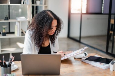 İş kadını, bilgisayarını modern bir ofiste araştırmaya hazır bir şekilde belgelerin analizine daldı..