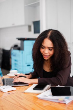 İş kadını, yoğun bir ofis masasında hesap makinesi ve dizüstü bilgisayarla çalışırken finansal verileri analiz ediyor..