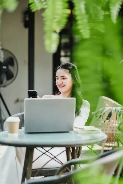 Usmívající Mladá Žena Užívá Kontrolu Svého Smartphonu Zatímco Sedí Notebookem Stock Fotografie