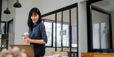 Gülümseyen genç bir profesyonel masasında kahve molası veriyor, rahat ve mutlu bir tavır sergiliyor..