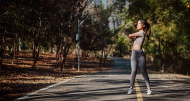 Ormanlık bir alanda kol çapraz hareketi yapan spor odaklı kadın esnekliğini artırıyor ve doğanın tadını çıkarıyor..