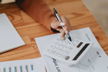 Finansal tablolar ve veriler üzerinde hesap makinesi kullanan bir iş adamının yakın plan görüntüsü, ayrıntılı analizi işaret ediyor..