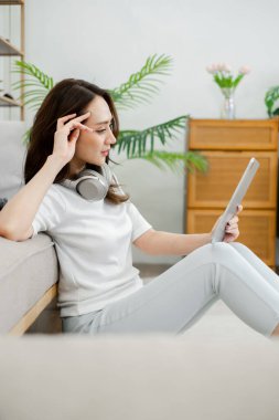 Düşünceli kadın bitki süslü, rahat oturma odasında kulaklık takarken tabletle meşgul oluyor..