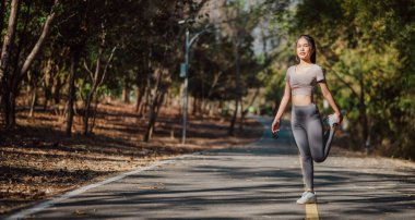 Bir kadın yolda geriniyor. Gri bir gömlek ve gri pantolon giyiyor. Yol boş ve etrafta başka kimse yok.