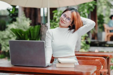 Gözlük takan bir kadın bir dizüstü bilgisayar ve bir yığın kitapla bir masada oturuyor. İşine odaklanmış durumda, muhtemelen bir proje üzerinde çalışıyor veya çalışıyor. Verimlilik ve konsantrasyon kavramı